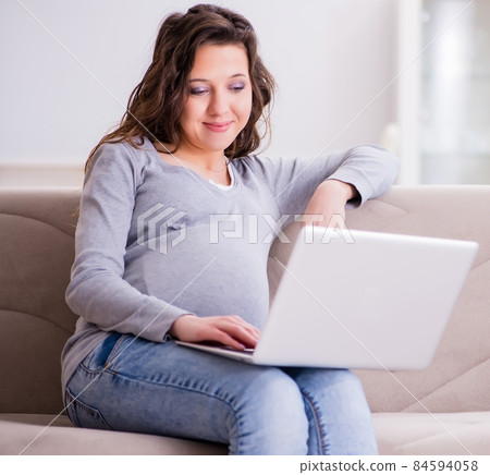 Pregnant woman working on laptop sitting on sofa Pregnant woman working on laptop sitting on sofa 84594058