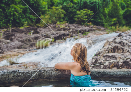 Geothermal spa. Woman relaxing in hot spring pool against the background of a waterfall 84594762