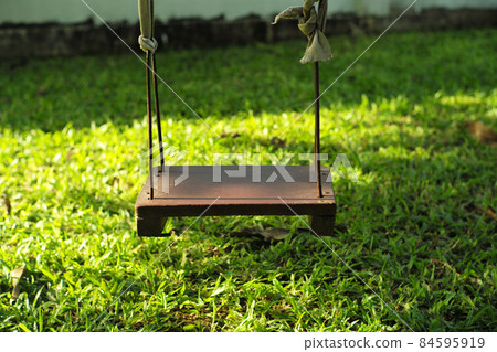 Closeup old wooden swing hanging from the tree in the backyard garden 84595919
