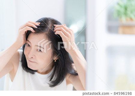 Middle-aged woman checking her hair while looking in the mirror 84596198