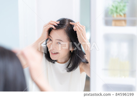 Middle-aged woman checking her hair while looking in the mirror 84596199