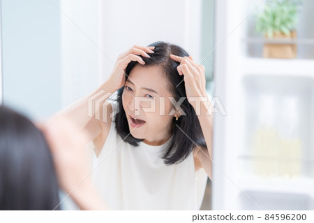 A middle-aged woman who is shocked by thinning hair looking in the mirror 84596200