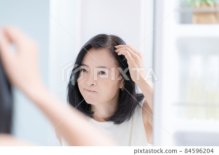 中年婦女一邊照鏡子一邊檢查頭髮 84596204