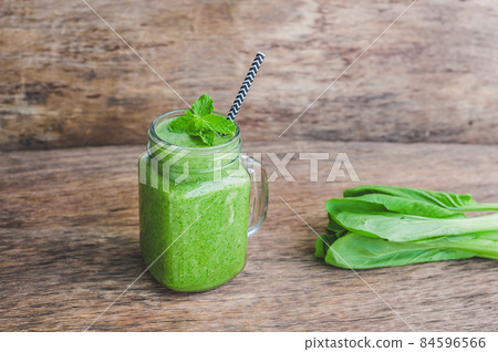 Mason jar mugs filled with green spinach, banana and coconut milk health smoothie with with a spoon of oatmeal on wooden rustic table 84596566