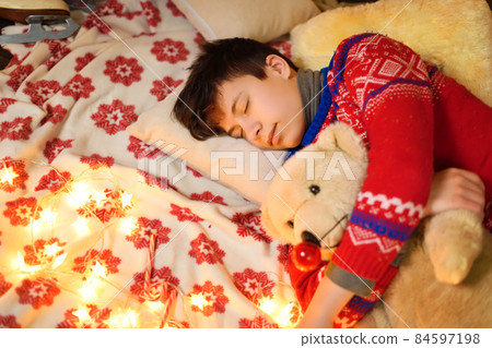 Boy sleeping in new year or christmas decoration. Holiday lights, gifts and christmas tree decorated with toys. 84597198