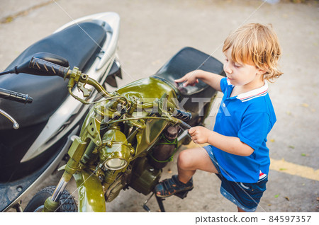 Cute blond boy looking at vintage motorcycle eatables new motorbike 84597357