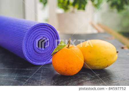 Yoga mat, water, orange and mango on a wooden background. Equipment for yoga. Concept healthy lifestyle, diet and sport. Copy space. Selective focus 84597752