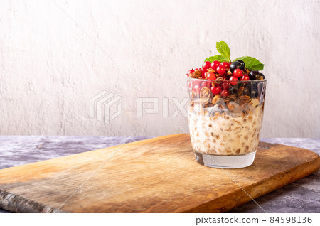 Granola with berries and yoghurt. Glass with granola on a cutting board. Copy space. Granola with berries and yoghurt. Glass with granola on a cutting board. Copy space. 84598136