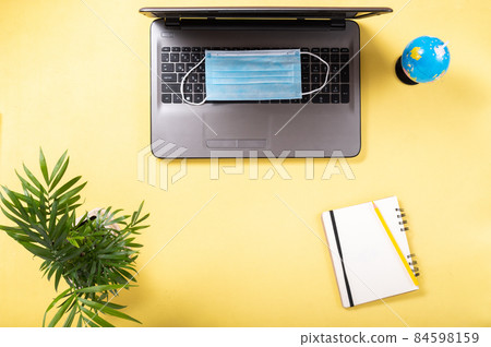 Laptop and medical mask. Choosing a country for tourism. Laptop and notepad. Ban on tourism. Top view. 84598159