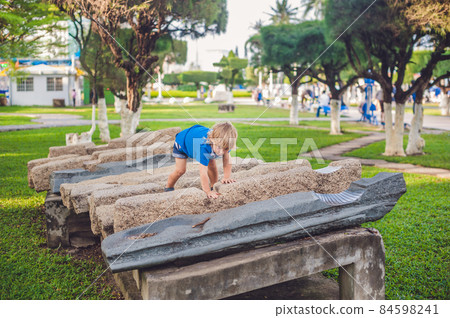 Cute blond boy climbs up the stone blocks on the playground. Childhood, concept Cute blond boy climbs up the stone blocks on the playground. Childhood, concept 84598241