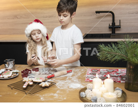 Children - a boy and a girl are preparing gingerbread in the kitchen Children - a boy and a girl are preparing gingerbread in the kitchen 84602001