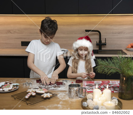 Children - a boy and a girl are preparing gingerbread in the kitchen Children - a boy and a girl are preparing gingerbread in the kitchen 84602002