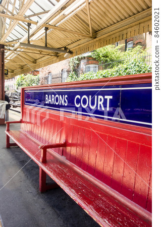London Underground station on the ground, Barons Court station platform with red bench London Underground station on the ground, Barons Court station platform with red bench 84602021