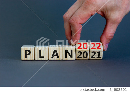 2022 plan new year symbol. Businessman turns a wooden cube and changes words 'Plan 2021' to 'Plan 2022'. Beautiful grey background, copy space. Business, 2022 plan new year concept. 2022 plan new year symbol. Businessman turns a wooden cube and changes words 'Plan 2021' to 'Plan 2022'. Beautiful grey background, copy space. Business, 2022 plan new year concept. 84602801