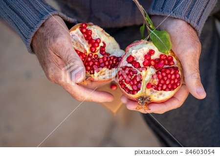 Ripe organic broken pomegranate, cut in half in senior hands .Selective focus,top view. Ripe organic broken pomegranate, cut in half in senior hands .Selective focus,top view. 84603054