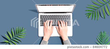 Person using a laptop computer with tropical leaves Person using a laptop computer with tropical leaves 84604772