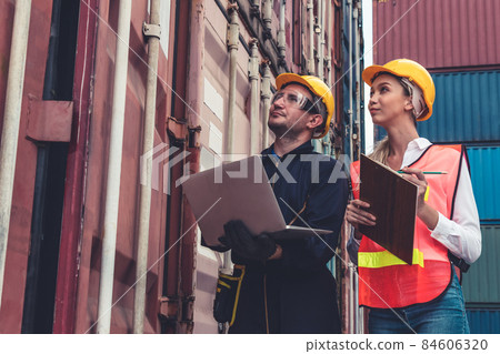 Industrial worker works with co-worker at overseas shipping container yard Industrial worker works with co-worker at overseas shipping container yard 84606320