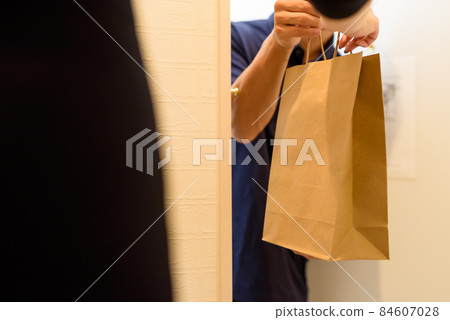 A male deliveryman who delivers food with a food delivery service and a female who receives it. 84607028