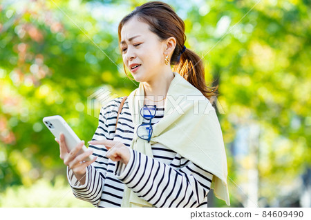 A woman looking at a smartphone with a troubled expression A woman looking at a smartphone with a troubled expression 84609490