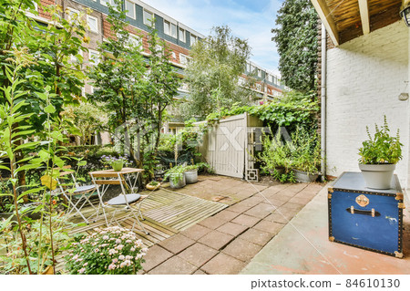 Green backyard of a house with wooden table and chairs and blue chest Green backyard of a house with wooden table and chairs and blue chest 84610130