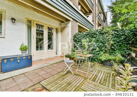 Green backyard of a house with wooden table and chairs and blue chest Green backyard of a house with wooden table and chairs and blue chest 84610131