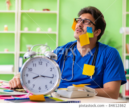 Young doctor sitting in hospital with many conflicting prioritie 84612862