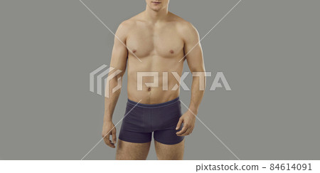Young man posing topless in underwear. Cropped faceless shot of male model with fit, muscular body wearing comfortable cotton underpants standing isolated on gray background. Male underwear concept 84614091