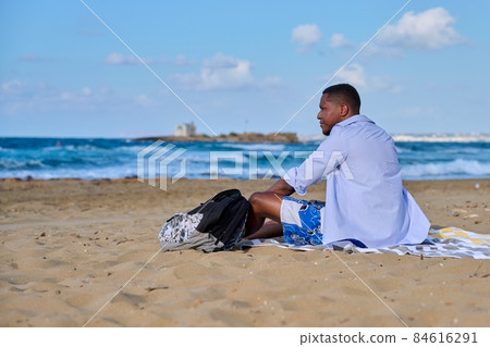 Young positive male tourist sitting resting on the beach Young positive male tourist sitting resting on the beach 84616291