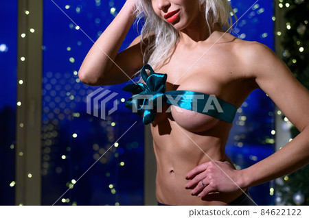 Nude Caucasian woman with turquoise boobs bow in front of Christmas decorations. Erotic gift. Nude Caucasian woman with turquoise boobs bow in front of Christmas decorations. Erotic gift. 84622122