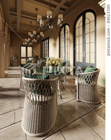 A wicker dining table with glass top and wicker chairs on a pillared terrace in the evening sun. A wicker dining table with glass top and wicker chairs on a pillared terrace in the evening sun. 84623380