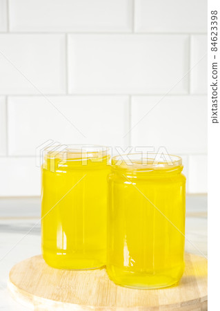 Two jars of clarified ghee butter on kitchen tile background, wooden plank. 84623398