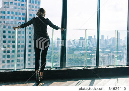 A young business woman is looking out the window from a hotel lobby. She is looking at the city view behind her thinking about her next project. She is point her finger up in the air. A young business woman is looking out the window from a hotel lobby. She is looking at the city view behind her thinking about her next project. She is point her finger up in the air. 84624440