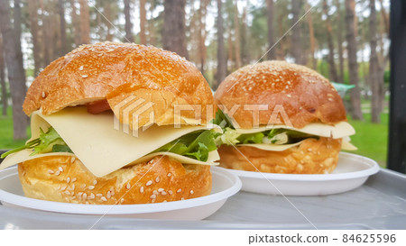 Close-up of two large DIY hamburgers in the park on a barbecue, rest and cooking on a picnic in the summer, food, delicious, bright colors. Unhealthy food concept. Fast food. Close-up of two large DIY hamburgers in the park on a barbecue, rest and cooking on a picnic in the summer, food, delicious, bright colors. Unhealthy food concept. Fast food. 84625596
