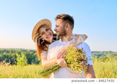 Happy middle-aged couple in love embracing, with a bouquet of wildflowers, 84627430