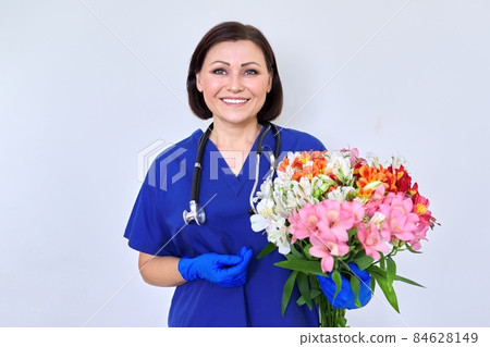 Woman doctor, nurse in blue with bouquet of flowers, on light background Woman doctor, nurse in blue with bouquet of flowers, on light background 84628149