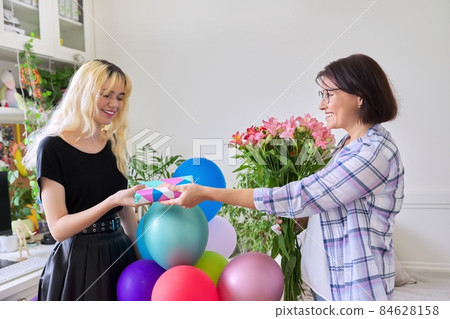 Mom congratulating her teenage daughter with gift flowers, at home in room Mom congratulating her teenage daughter with gift flowers, at home in room 84628158