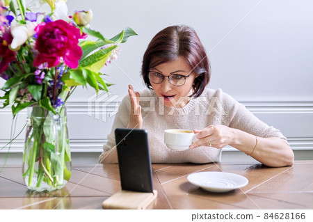 Middle-aged woman sitting at home using smartphone for video call 84628166