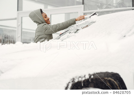 Woman removing snow from car windshield 84628705