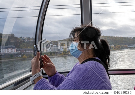 A middle-aged Asian woman with a smartphone wearing face mask in a cable car A middle-aged Asian woman with a smartphone wearing face mask in a cable car 84629025