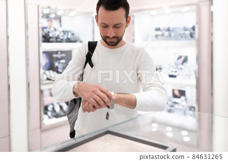 Photo of an adult handsome brunette man in a white sweatshirt chooses and tries on a stylish wrist 84631265