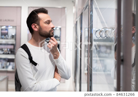 Photo of an adult handsome brunette man in a white sweatshirt and with a backpack chooses a stylish 84631266