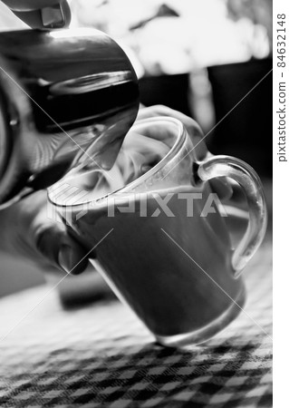 man pouring coffee into a cup of milk in black and white 84632148