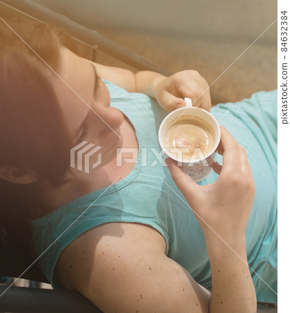 young caucasian happy woman drinking coffee in sunlight, top view young caucasian happy woman drinking coffee in sunlight, top view 84632384