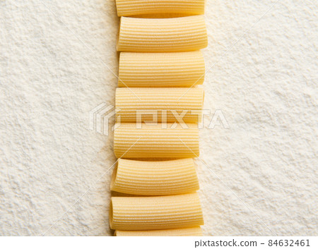 Flat lay composition of neatly arranged whole wheat Italian pasta in a row on a floured surface with copy space for ad 84632461