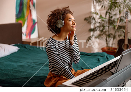 Smiling woman sitting near synthesizer at home 84633664