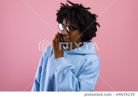 Portrait of black teenage guy whispering secret, sharing confidential information, spreading gossip on pink background 84634239