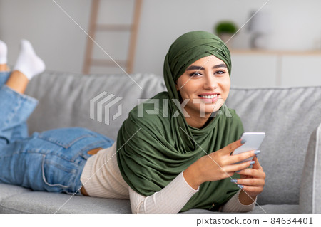 Arab woman in hijab lying on sofa, using mobile phone, checking social network, browsing web, communicating online Arab woman in hijab lying on sofa, using mobile phone, checking social network, browsing web, communicating online 84634401