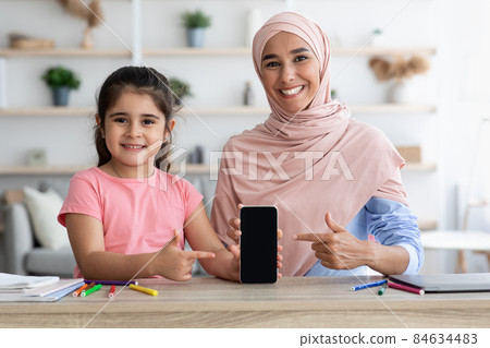 Great App. Little Girl And Muslim Mom Pointing At Blank Smartphone, Mockup 84634483