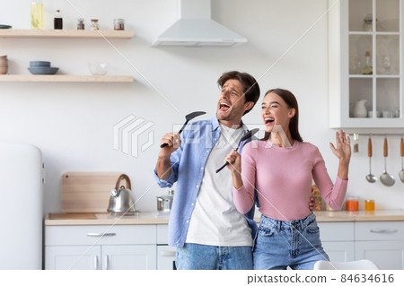 Smiling young caucasian male and female have fun, sing song at microphone, prepare food 84634616