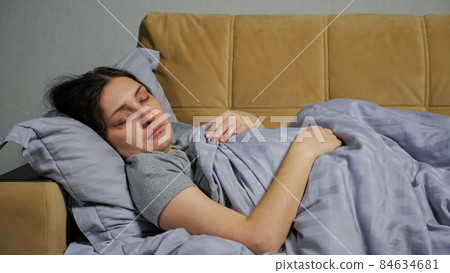 Sick young woman lies on couch under blanket and coughs 84634681